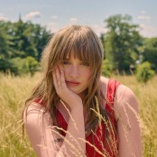 A woman in a red top with brown hair sat in a field